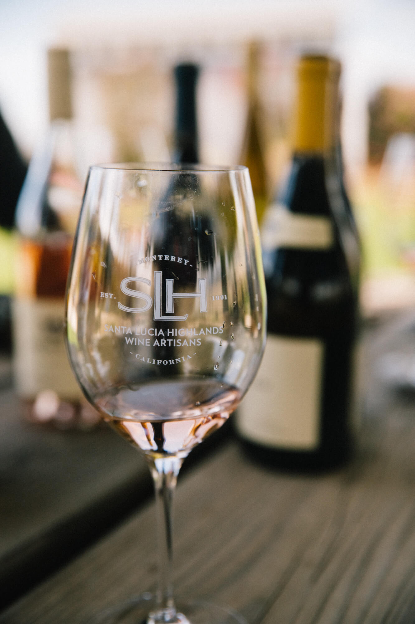 Wine glass with Santa Lucia Highlands logo and rosé, bottles in background.