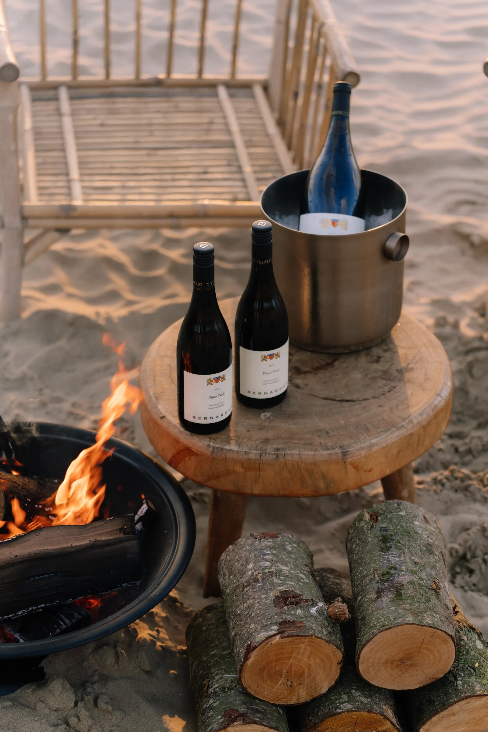 Santa Lucia Highlands wine bottles by a beach bonfire and bamboo chair.