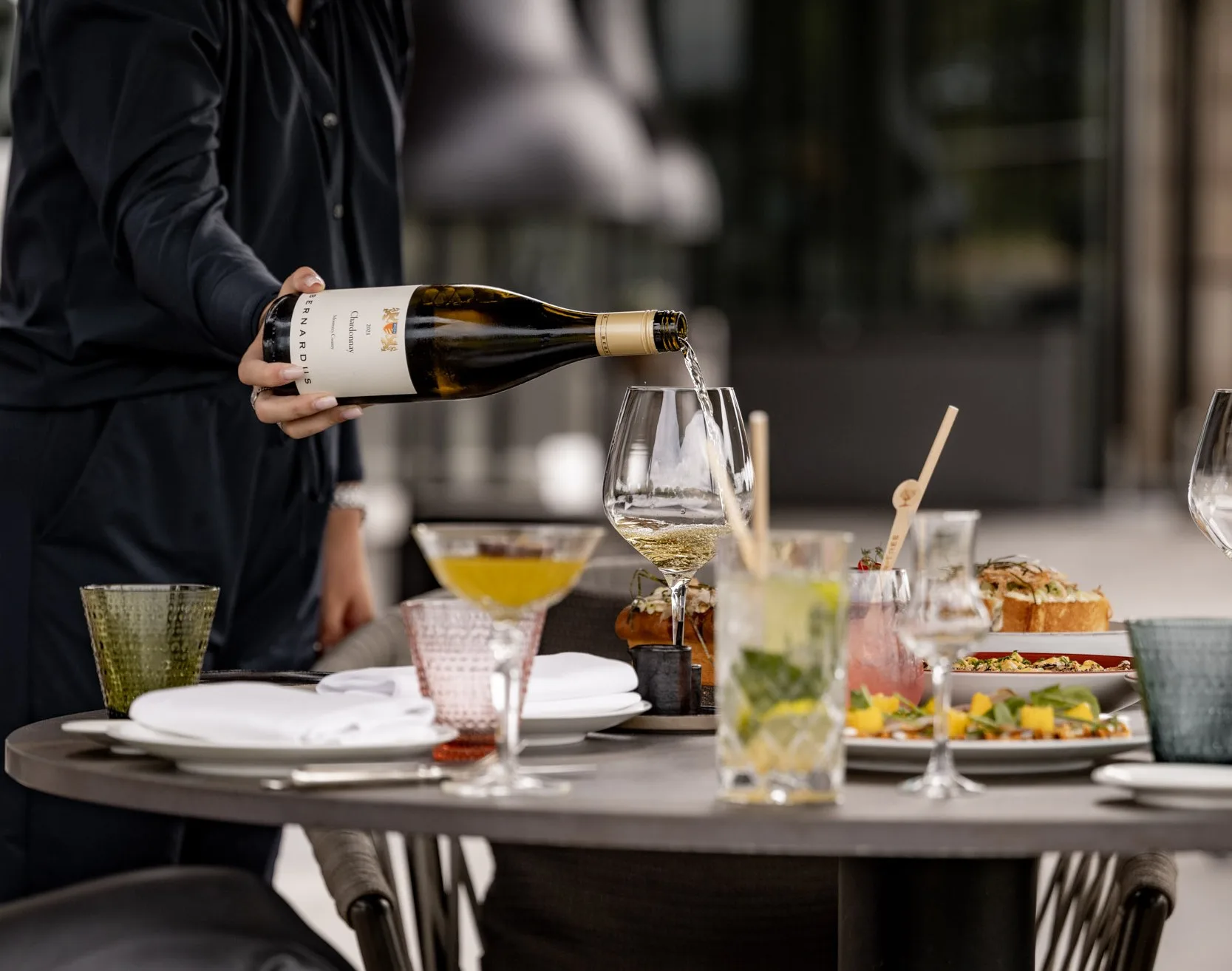 Server pouring white wine at a table with food and drinks in Santa Lucia Highlands.