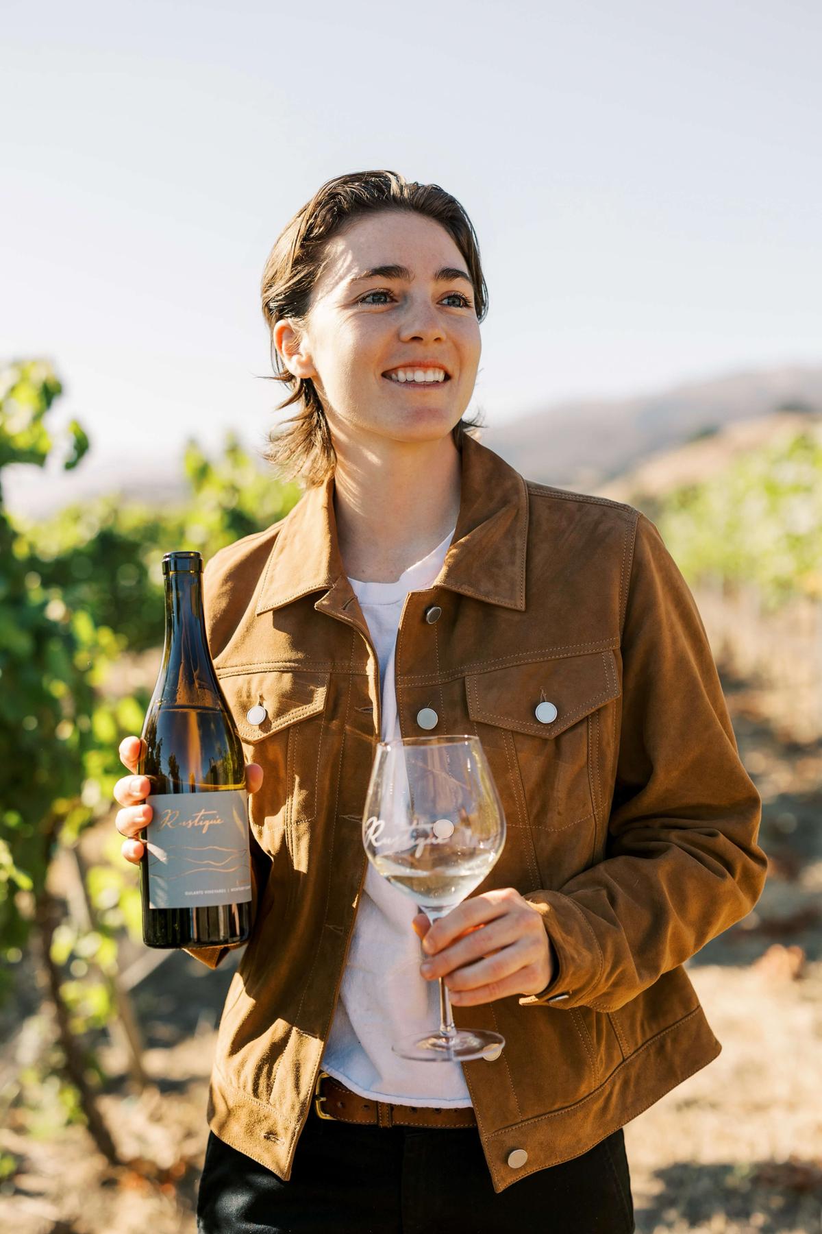 Sara Rustique, winemaker, holding a bottle and glass of wine in Santa Lucia Highlands vineyards.