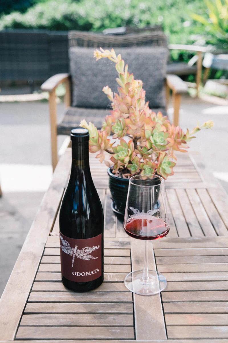 Bottle of Odonata wine and glass on a table with a succulent and chairs.