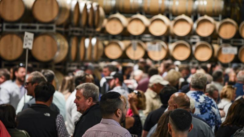 Crowd of people at a Santa Lucia Highlands wine event with wine barrels in the background.