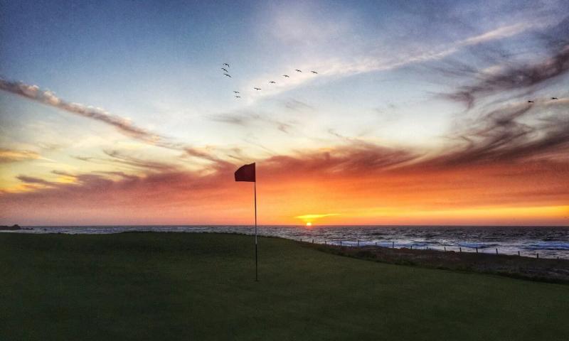 Golf course green with red flag at sunset over the Pacific Ocean at Pebble Beach, California.