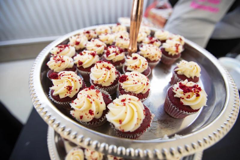 Red velvet cupcakes with cream cheese frosting and red velvet crumbles on a silver tiered stand.