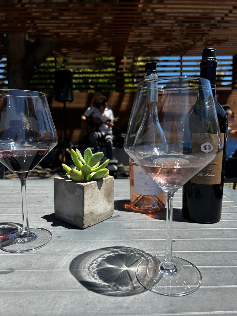 Two glasses of wine and bottles on a table with a musician playing guitar in the background.
