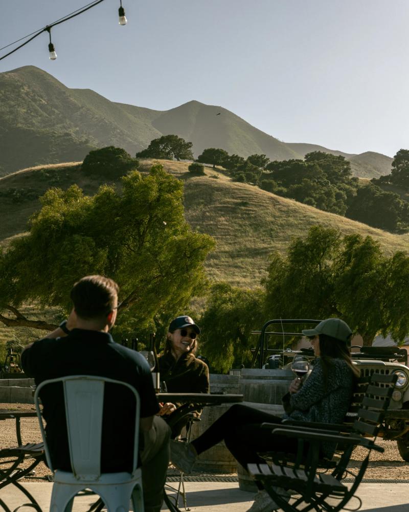 People enjoy wine tasting outdoors with rolling hills and vineyards in the Santa Lucia Highlands.