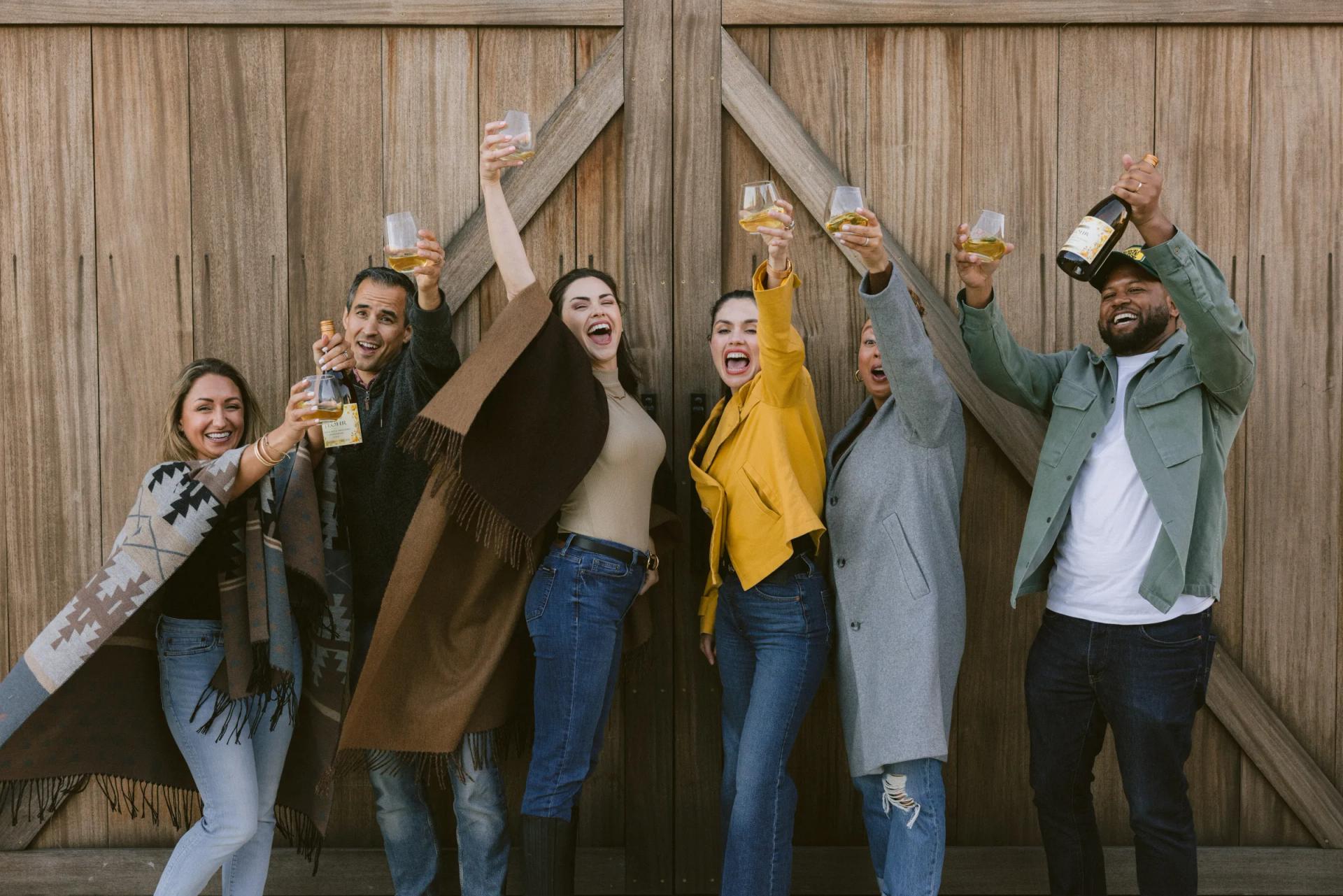 Group of friends toasting with wine in front of a rustic wooden barn in Santa Lucia Highlands.