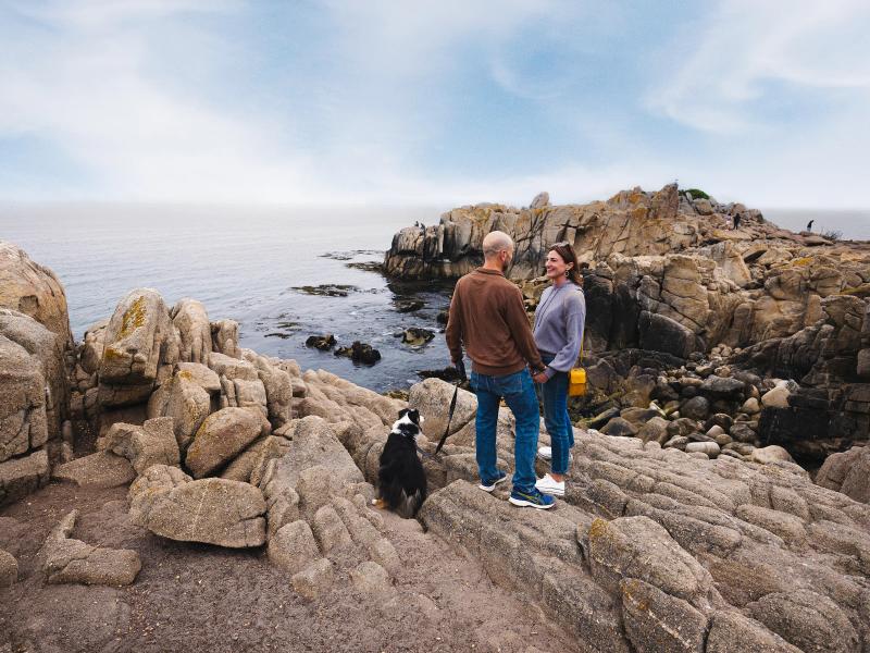 Couple and dog on rocky coast near Pacific Grove, Monterey County, California.