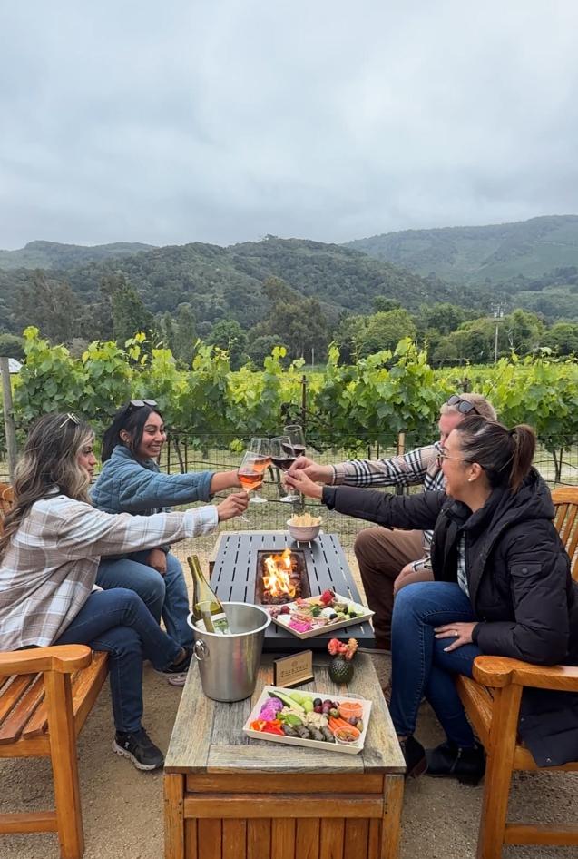 Friends toast wine by a fire pit at Folktale Winery in Carmel Valley, Monterey County.