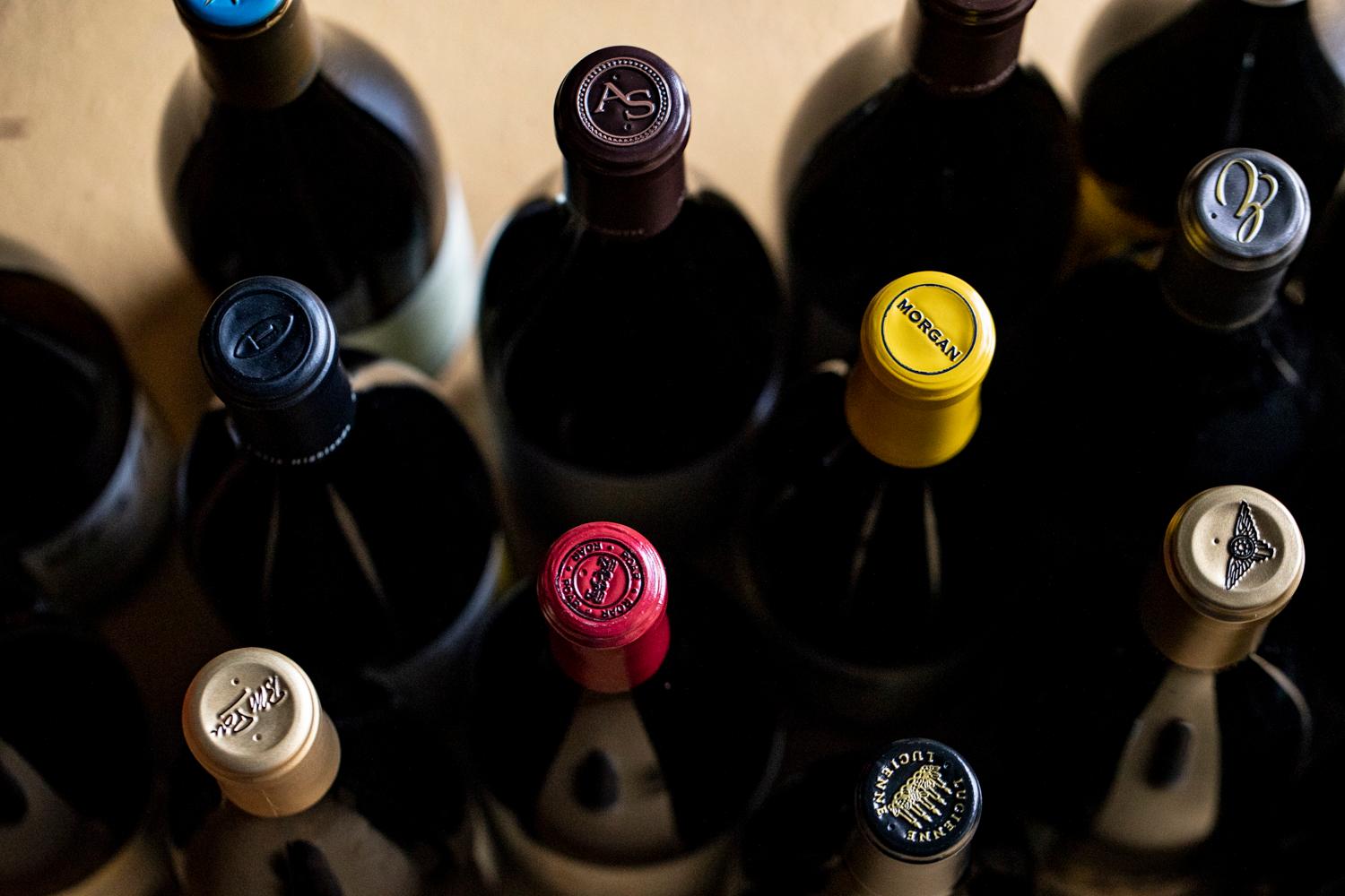 Assortment of wine bottles with various colored caps and embossed logos from Santa Lucia Highlands wineries.