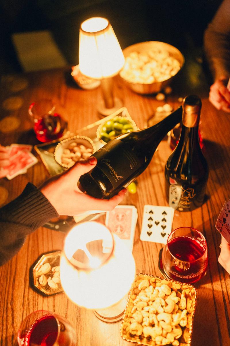 Caraccioli Cellars wine bottle and glasses on a table with playing cards and snacks.
