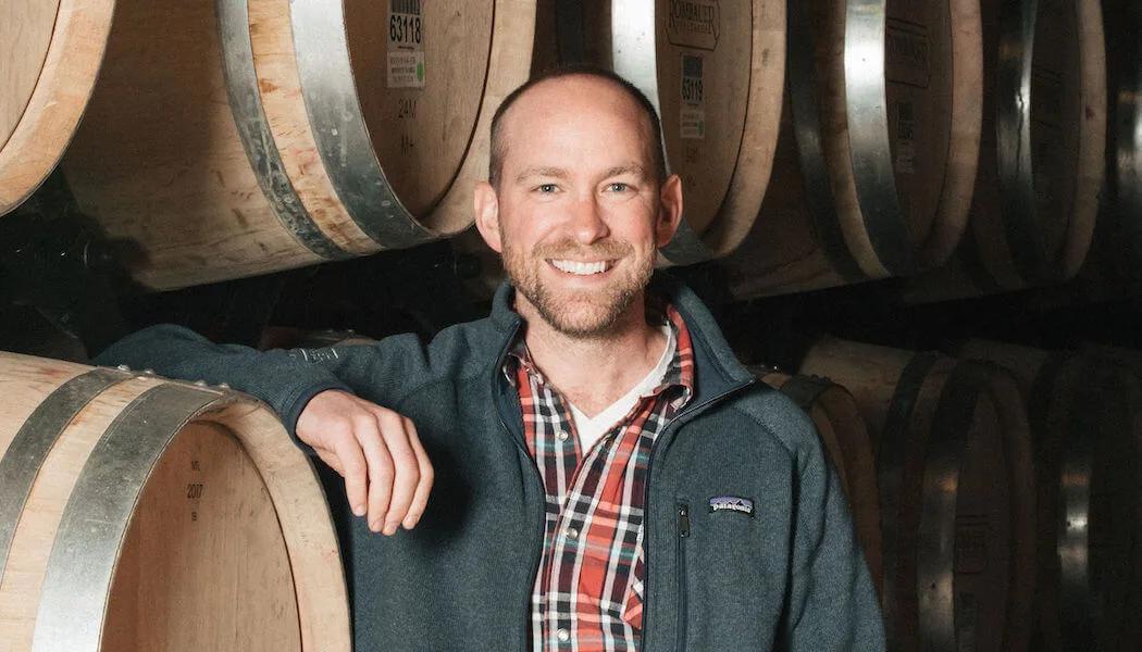 Richie Allen smiles in a wine cellar, leaning on barrels in Santa Lucia Highlands.