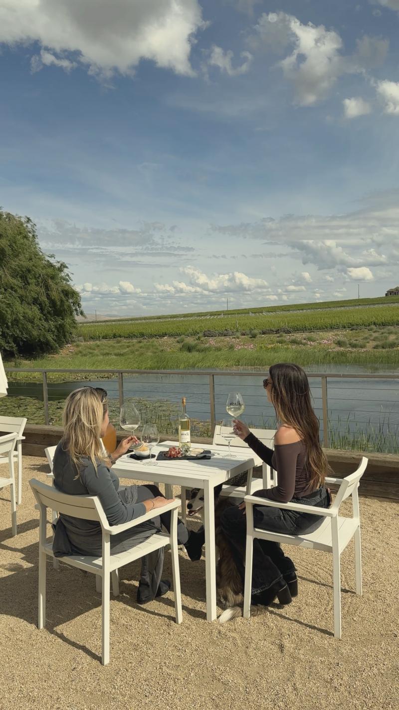 Two women toast with wine at a table overlooking vineyards at Wrath Wines tasting room in Santa Lucia Highlands at Wrath Winery Tasting Room on River Road.
