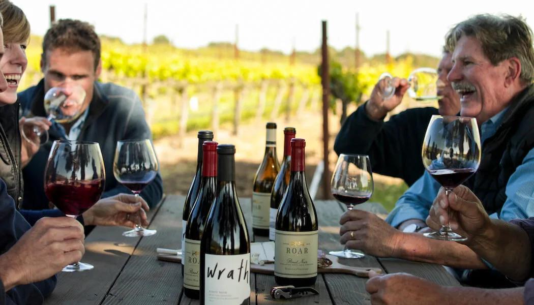 People enjoying wine tasting at a table in a Santa Lucia Highlands vineyard.